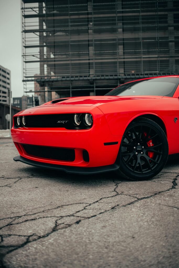 Close-up of a red Dodge Challenger parked on urban concrete pavement, showcasing luxury and sports car appeal.